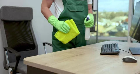 Cleaner in green uniform wiping office desk during commercial cleaning service