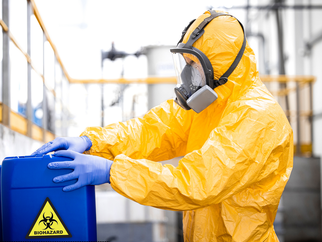 Technician in yellow hazmat suit safely handling biohazard sharps container during needle sweep cleanup
