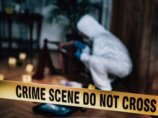 Crime scene cleaner in protective suit behind crime scene tape during trauma clean up.